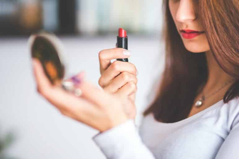 travel beauty - woman applying red lipstick 
